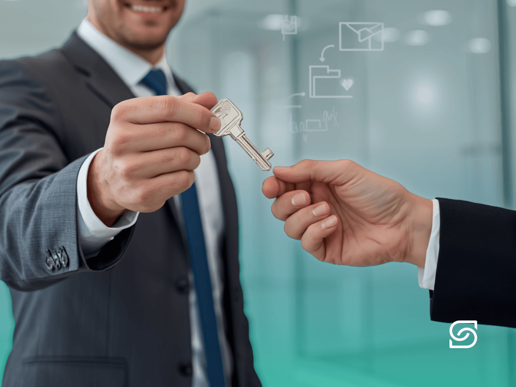 Close-up of a businessman in a grey suit handing a silver key to another person's outstretched hand, with faint email and folder icons in the background.