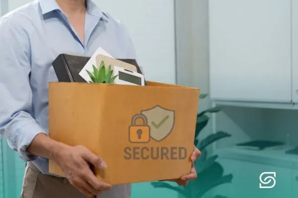 Employee carrying a cardboard box of office belongings marked with a security shield and padlock icon.