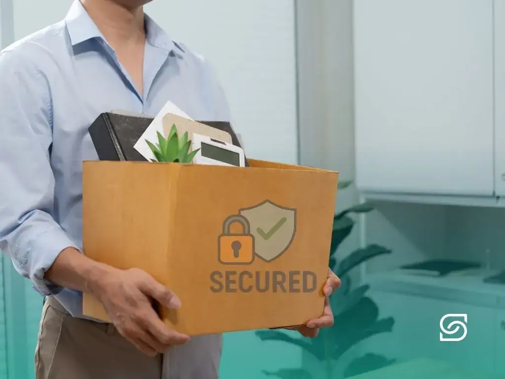 Employee carrying a cardboard box of office belongings marked with a security shield and padlock icon.