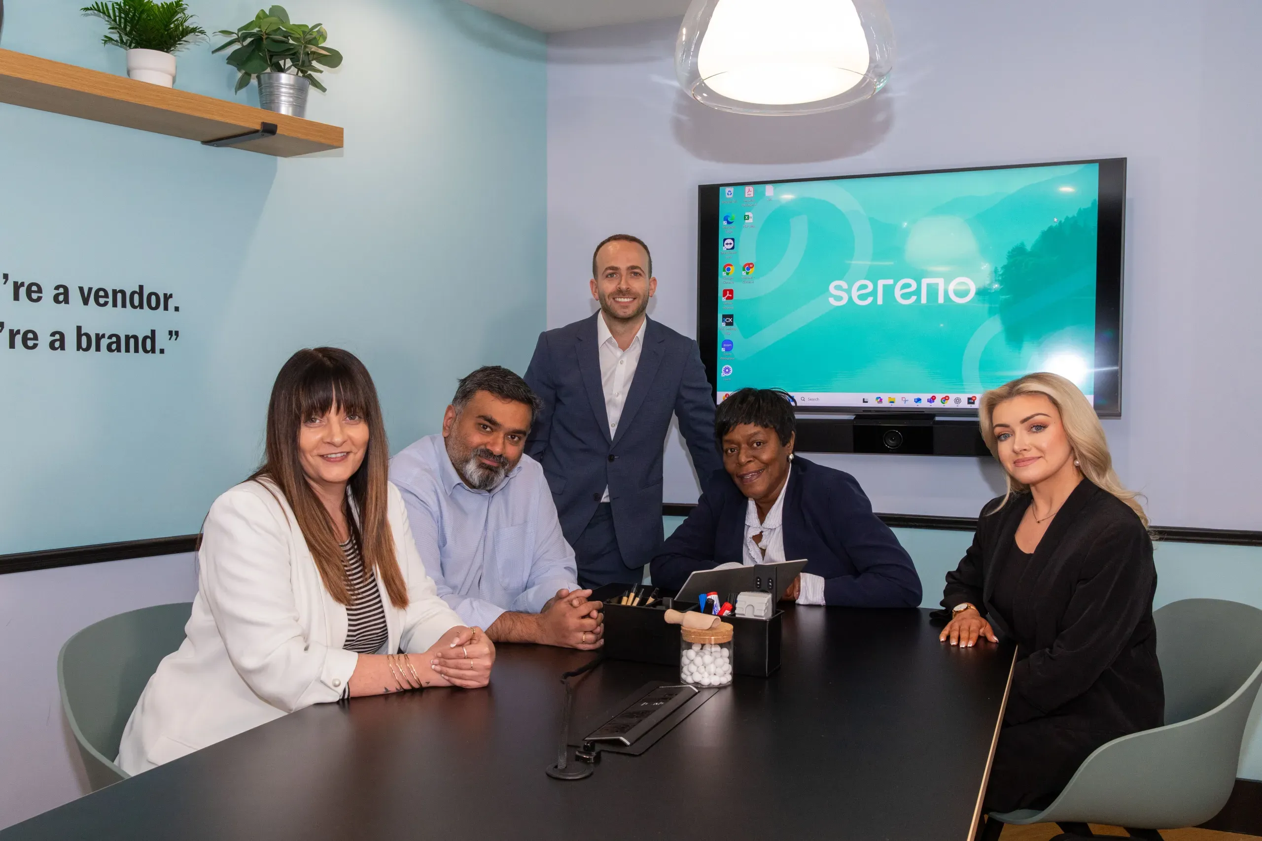 The Sereno IT team gathered in their London office meeting room beside a screen showing the Sereno brand